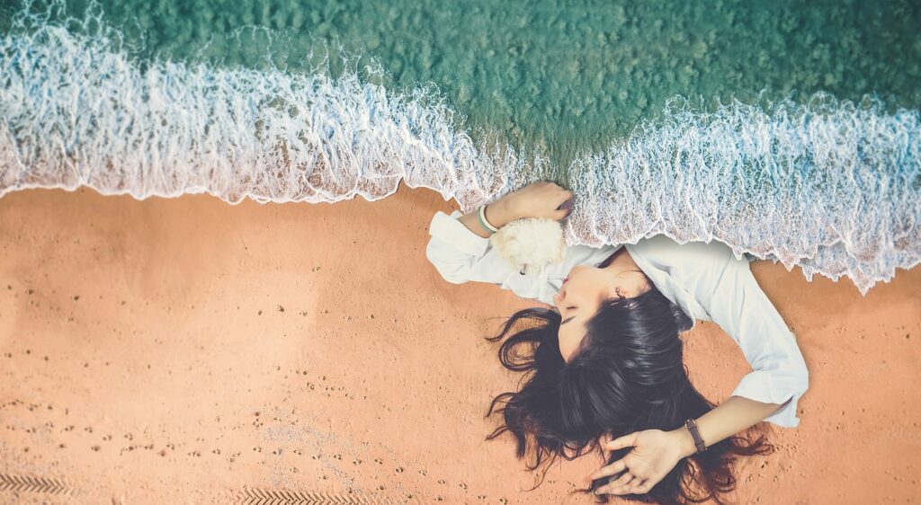 A person sleeping on a beach with the gentle waves lapping against them like a duvet cover pulled up.