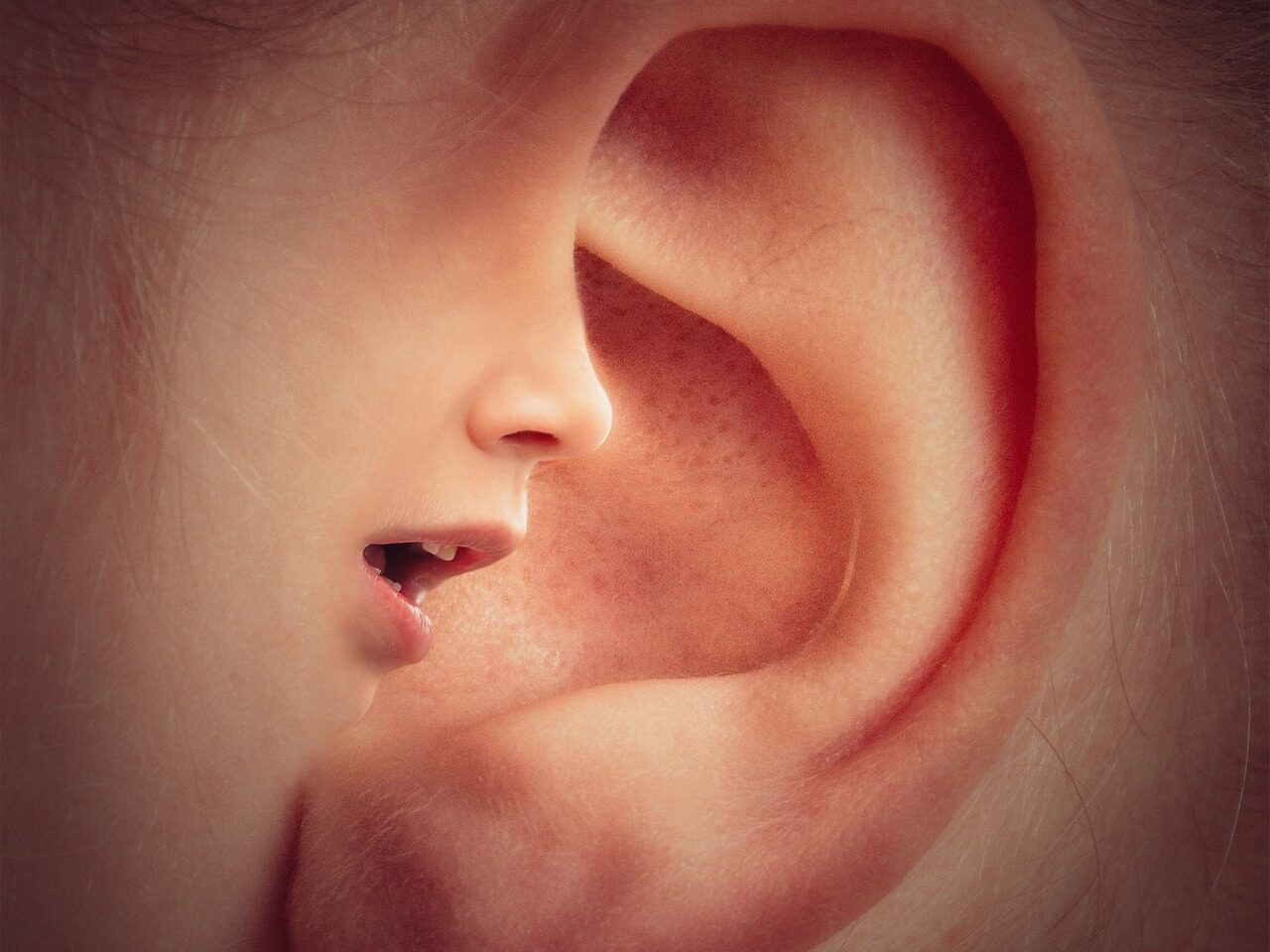 A close up ear with part of the ear forming a child's face speaking into it.