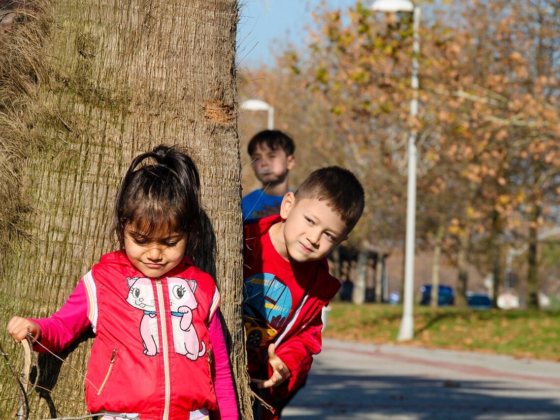 Three children playing around the base of a tree.